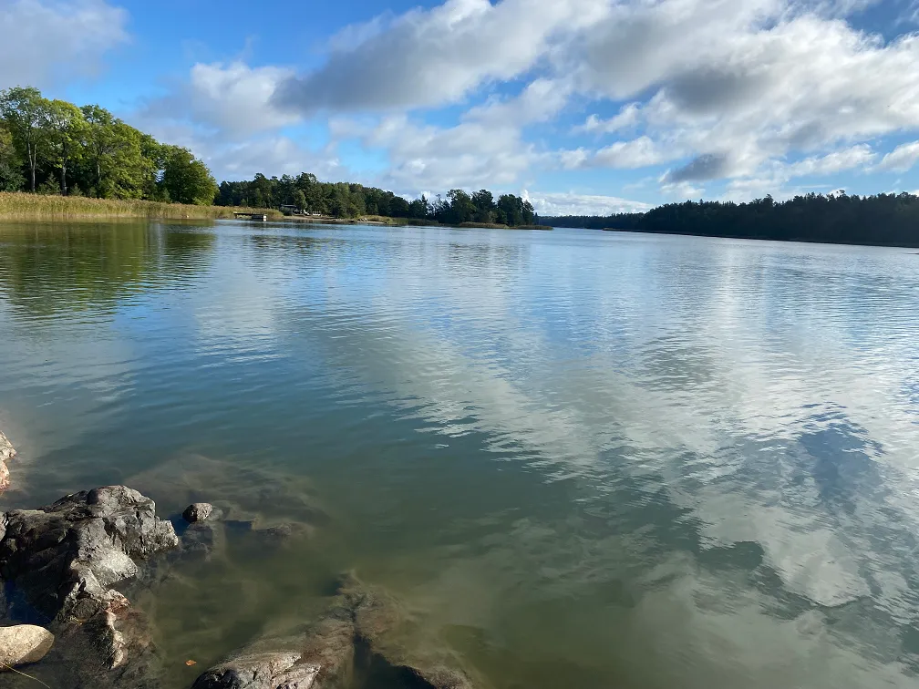Utsikt över en sjö med klippor i förgrunden och moln på himlen.